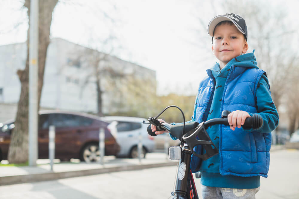 Child on the sidewalk holding a bicycle.